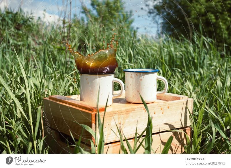 Emailbecher auf einer Holzkiste mit spritzendem Getränk Frühling Gras Tee Außenaufnahme trinken Geplätscher heiß Tasse Emaille Kaffee Picknick wandern Sommer