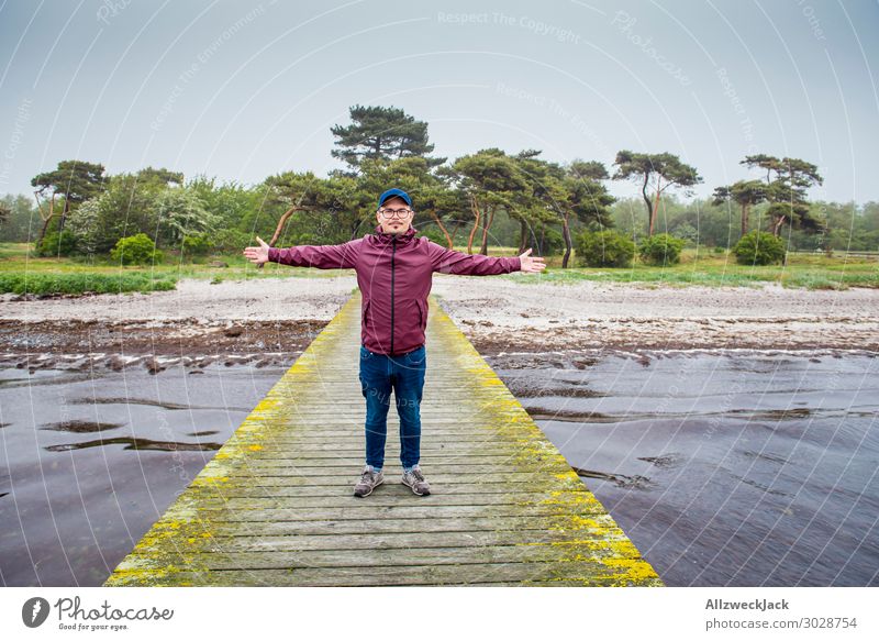 junger Mann in weinroter Regenjacke auf einem Steg Schweden Ostsee Küste maritim Wolken Nieselregen Ferien & Urlaub & Reisen Urlaubsort Urlaubsfoto Erholung
