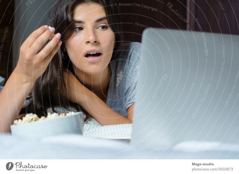 Junge Frau benutzt Laptop und isst Popcorn. Lifestyle Freude Glück schön Erholung Haus Schlafzimmer Entertainment Computer Notebook Technik & Technologie