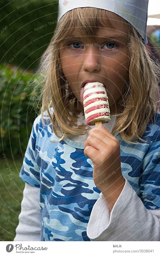 Blondes, langhaariges Mädchen mit Krone, hält Eis mit Kringel in der Hand und schleckt daran. Geburtstagsfeier zuhause im Garten. Lebensmittel Dessert Süßwaren