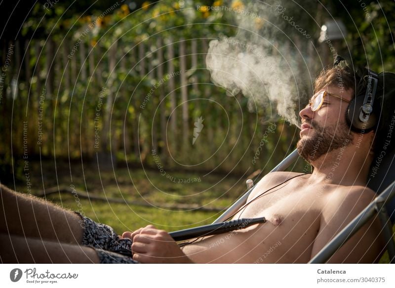 Relaxen, junger Mann mit Kopfhörer raucht im Liegestuhl Rauchen Rauschmittel Musik hören Natur Pflanze Sommer Schönes Wetter Blume Gras Blatt Blüte Sonnenblume
