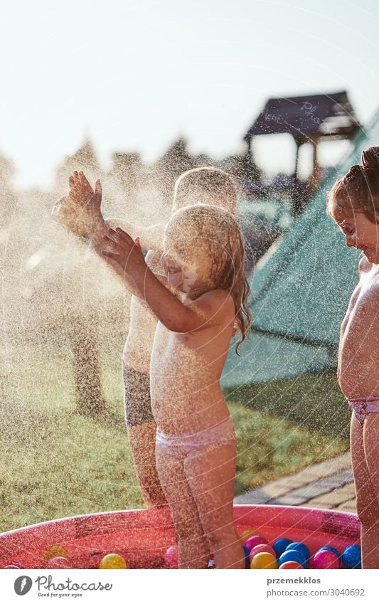 Kleine Kinder genießen ein kaltes Wasser, das von ihrem Vater gesprüht wird. Lifestyle Freude Glück Erholung Schwimmbad Ferien & Urlaub & Reisen Sommer