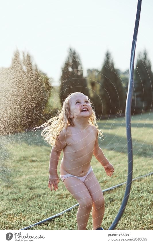 Kleine niedliche adorable Mädchen genießen ein kühles Wasser von ihrer Mutter während heißen Sommertag im Hinterhof gesprüht. Unverfälschte Menschen, echte Momente, authentische Situationen
