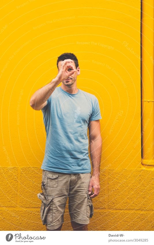 junger Mann formt vor einer gelben Wand das Zeichen für exzellent Hand Blick korrekt perfekt ausdruck Zeichensprache richtig positiv super ausdrucksstark