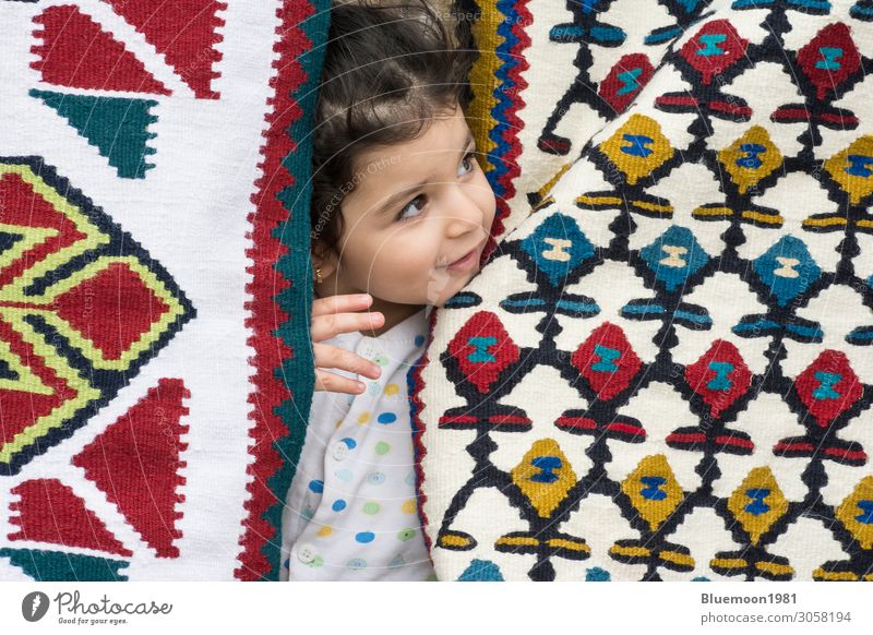 Nahaufnahme eines kleinen Mädchens zwischen Kelims mit traditionellen volkstümlichen geometrischen Mustern Reichtum Design stricken Kind 1-3 Jahre Kunst Kultur
