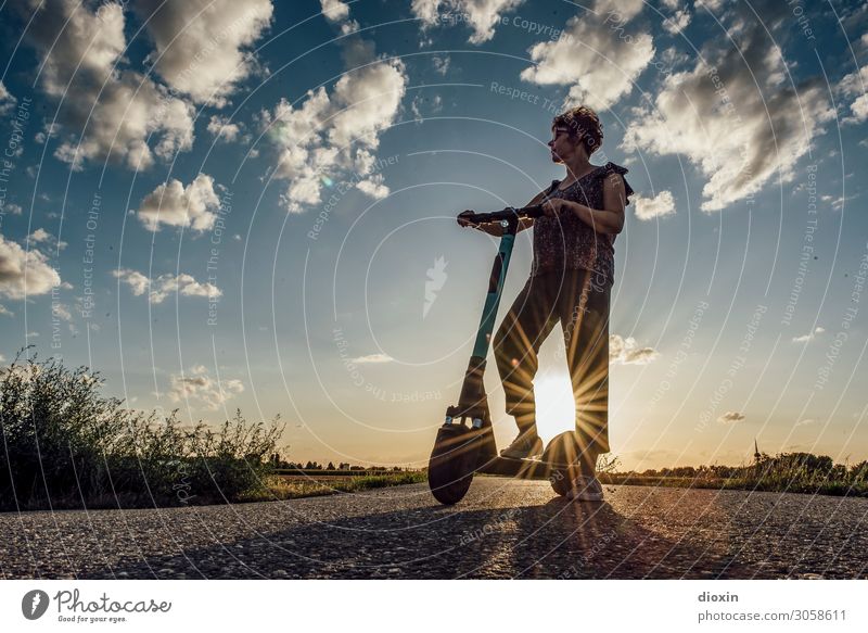 Frau mittleren Alters steht mit e-scooter vor untergehender Sonne und trotzt dem | Klimawandel E-Scooter Verkehrsmittel Mobilität Lifestyle Straßenverkehr