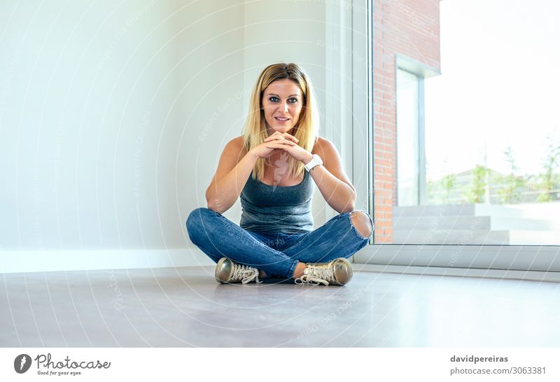 Nachdenkliches Mädchen, das in einem Wohnzimmer sitzt. schön Zufriedenheit Haus Mensch Frau Erwachsene Hand Jeanshose Turnschuh blond Holz beobachten Denken