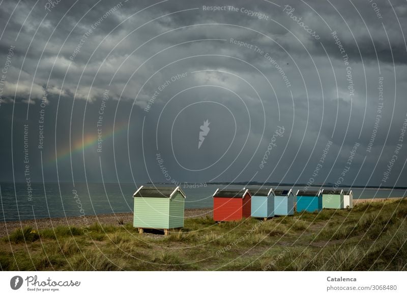 Eine Reihe bunter Strandhütten in den Dünen leuchten  als die Gewitterwolken auflockern und ein Regenbogen erscheint Meer Dünengras Horizont schlechtes Wetter