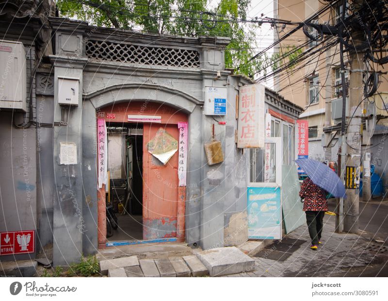 Routine in alten Gassen Pekings Ladengeschäft Leben schlechtes Wetter Stadtzentrum Fassade Hauseingang Regenschirm Schriftzeichen Hinweisschild authentisch