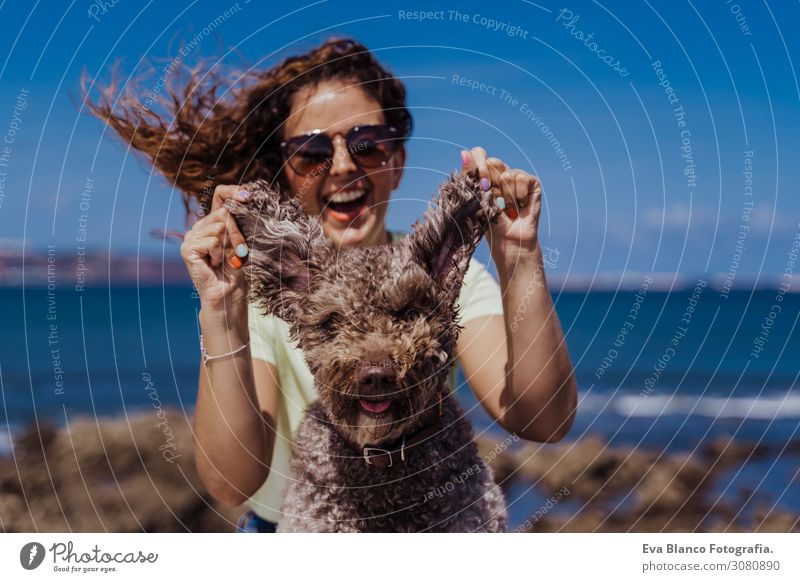 junge Frau und ihr süßer spanischer Wasserhund im Freien, die gemeinsam an einem sonnigen und windigen Tag genießen. Sommerzeit, Tierliebe und Ferienkonzept
