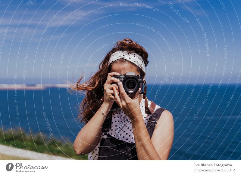 junge kaukasische Touristin, die an einem windigen und sonnigen Tag mit einer Spiegelreflexkamera im Freien fotografiert. Lebensstil, Reisen und Sommerzeit