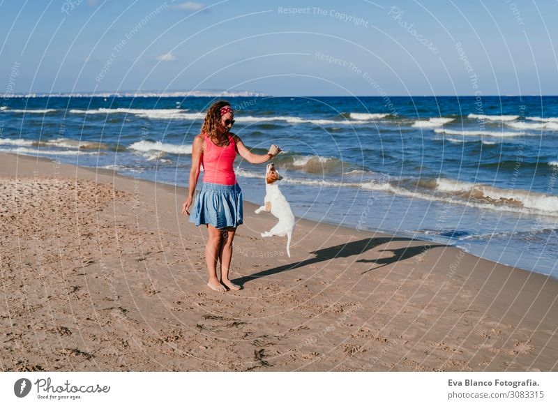 junge Frau und ihr süßer kleiner Jack-Russell-Terrier, die am Strand mit einem Tennisball spielen. Sommer- und Ferienkonzept Jugendliche Erholung blau