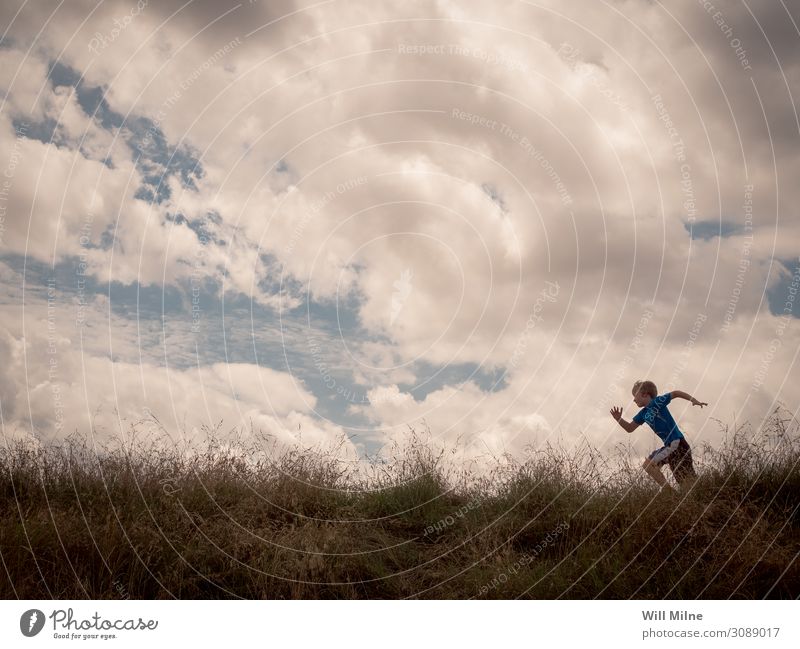Ein Junge rennt über den Gipfel eines Hügels. rennen Laufsport Läufer Wolken Himmel sehr wenige Textfreiraum üben Jugendliche Junger Mann Jugendkultur Kind Gras