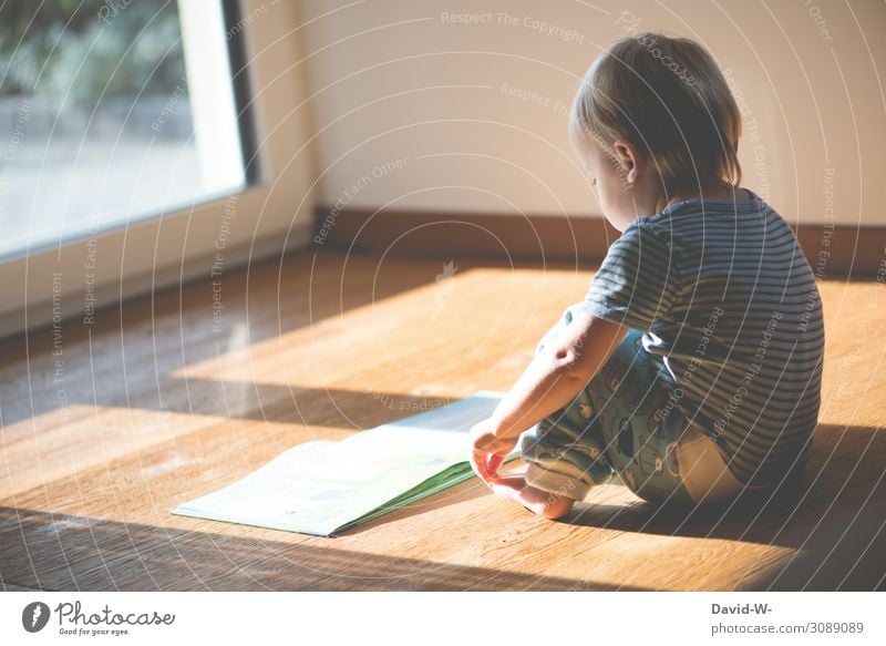 ein Kind sitzt auf dem Holzboden und liest ein Buch, während es von der Sonne angestrahlt wird Parkett lesen alleine zu hause selbstbeschäftigung ruhe