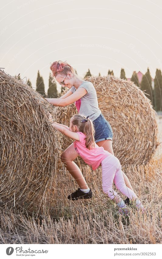 Schwestern, Teenager-Mädchen und ihre jüngere Schwester schieben Heuballen spielen zusammen im Freien auf dem Lande Lifestyle Freude Glück Erholung