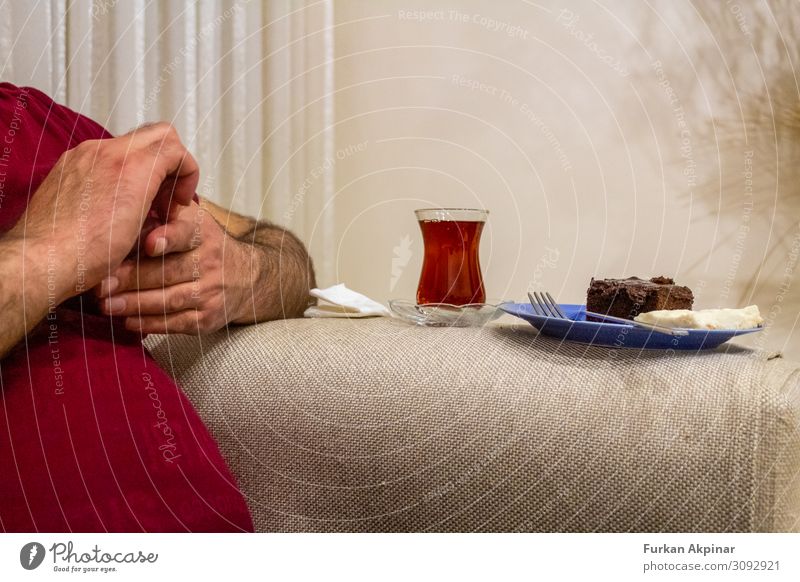 Bauchmann sitzt in der Hand, neben ihm Tee und Kuchen. Mensch Mann Erwachsene Arme Finger 30-45 Jahre Gesundheit mehrfarbig Vorderansicht