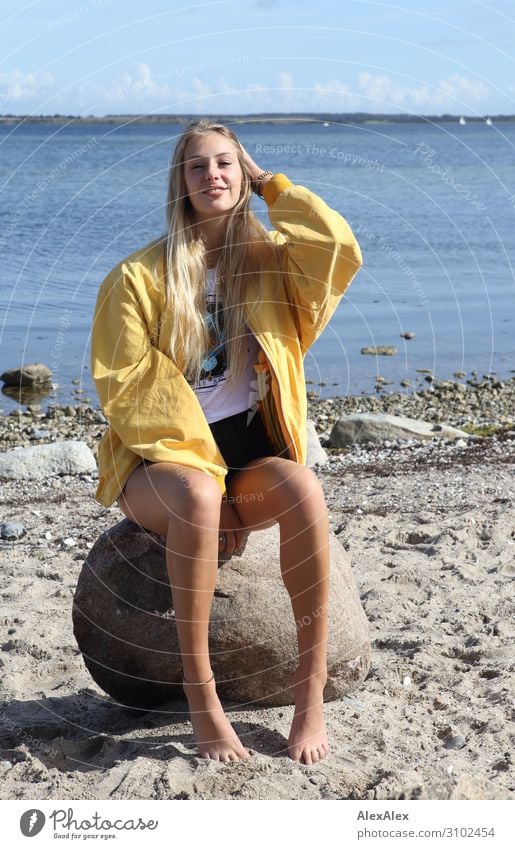 Junge Frau mit gelber Jacke auf einem Fels am Strand Stil Freude schön Leben Wohlgefühl Sommer Sommerurlaub Sonne Meer Jugendliche Beine 18-30 Jahre Erwachsene