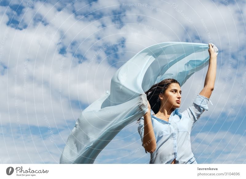 Junge Frau, die einen Schnitt aus blauem Stoff am Himmel hält. Luft Horizont Höhe Außenaufnahme attraktiv Sommer Natur Glück Erwachsene Einsamkeit Wolken