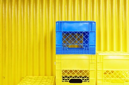 Gelbe und blaue Kisten vor einer gelben Wellblechwand kaufen Mauer Wand Fassade Kasten Kunststoff Behälter u. Gefäße Stapel Güterverkehr & Logistik tragen leer