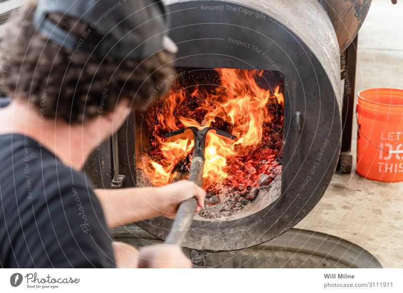 Mann schürt Feuer in einem Raucher Grill Grillen Grillplatz Fleisch Holz Flamme heiß heizen Schaufel schaufeln Essen zubereiten kochen & garen Koch Rauchen