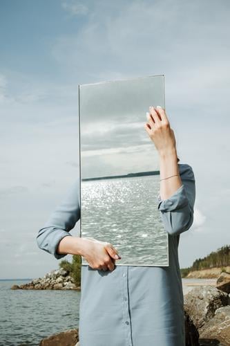 Frau steht auf einem Ufer in blauem Kleid und hält einen Spiegel. Erwachsene Sauberkeit Entwurf Umwelt gesichtslos Hand vertikal Natur Außenaufnahme