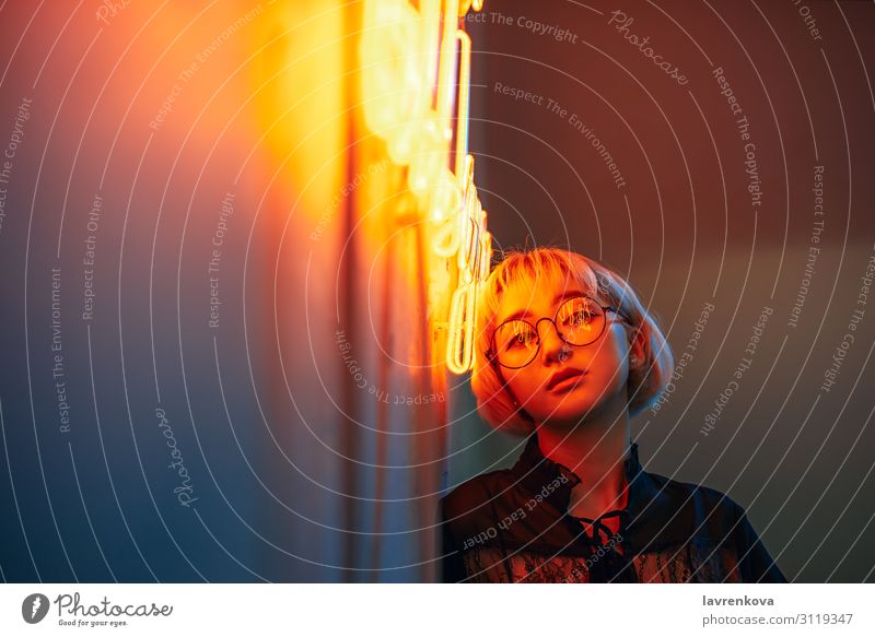 Junge erwachsene Asiatin mit Brille vor einem Neonlichtschild, flacher selektiver Fokus Asiate blond Frau Junge Frau Mädchen Beleuchtung Illumination Licht