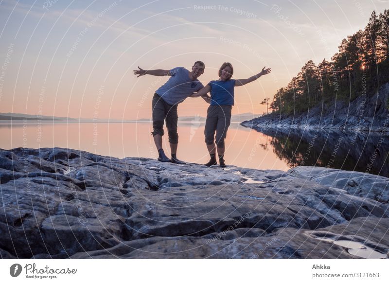 Junges Paar winkt fröhlich an einem windstillen See am Abend Partnerschaft Zuneigung Glück Zusammensein harmonisch Natur Windstille Felsen Skandinavien