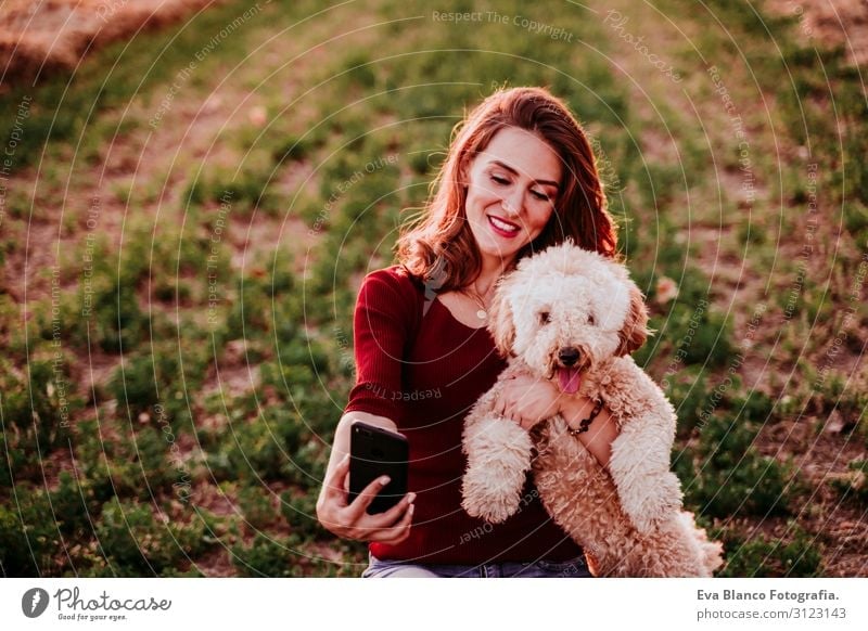 schöne kaukasische Frau, die bei Sonnenuntergang auf dem Land einen Selfie mit ihrem Hund mitnimmt. Mit dem Mobiltelefon. Technologie und Lebensstil im Freien