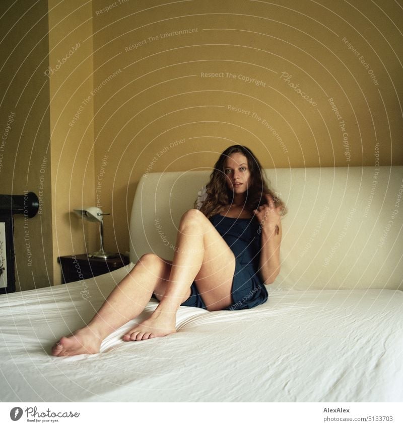 Portrait einer jungen Frau auf einem weißen Bett vor einer gelben Wand Stil schön Leben Häusliches Leben Junge Frau Jugendliche Beine 18-30 Jahre Erwachsene