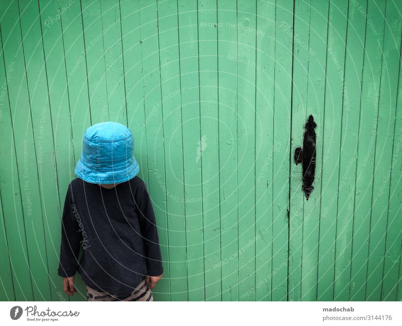 Kamerablick - Junge steht vor grüner Wand Textfreiraum Kleinkind Leben Mauer Fassade Tür Mütze Stimmung Verschwiegenheit ästhetisch Einsamkeit Enttäuschung