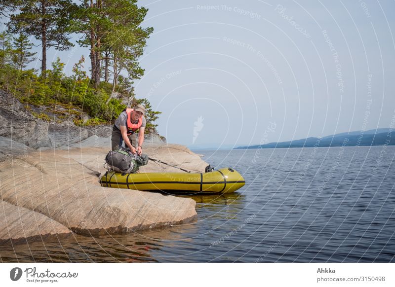 Junger Mann packt sein Boot am steinernen Ufer eines Sees Vorbereitung aufbruchstimmung sicherer Hafen Aufbruch Kajak Insel Bootsfahrt packen ufer vorbereiten