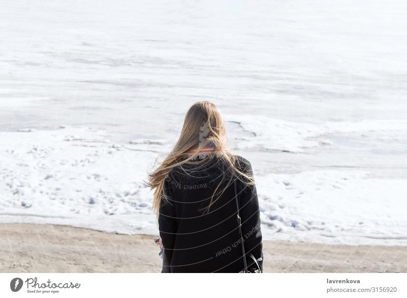 Rücken der jungen Frau, die auf dem zugefrorenen Fluss steht. gesichtslos Einsamkeit Küste Strand Schnee Eis kalt Ferien & Urlaub & Reisen blond Behaarung
