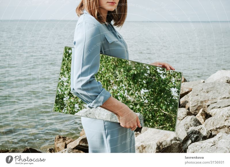 Wman steht an einem Ufer in blauem Kleid und hält einen Spiegel. Lifestyle Jugendliche 18-30 Jahre Junge Frau Sommer Erwachsene Sauberkeit Entwurf Umwelt