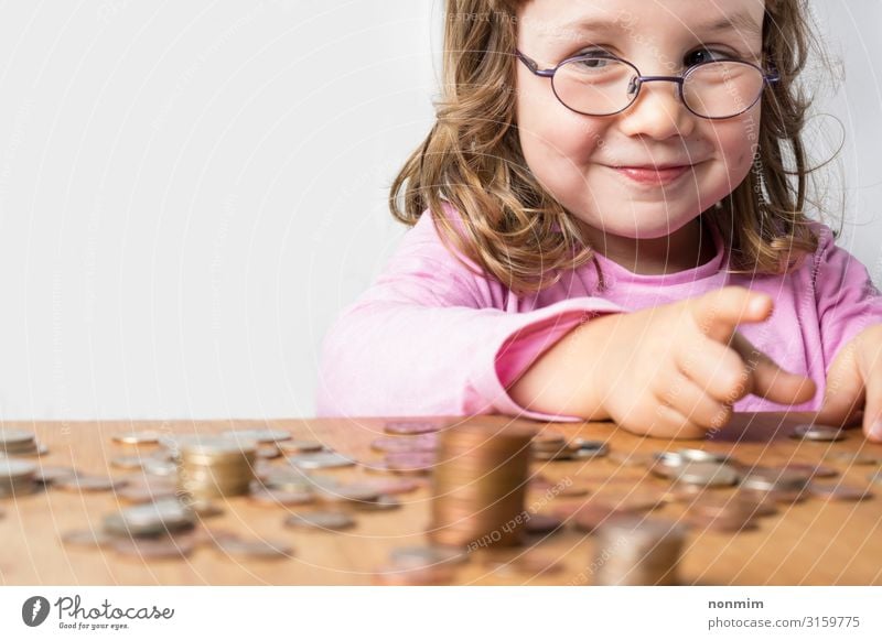 Lächelndes Mädchen mit Brille in rosa Kleidung, das Münzen für Ersparnisse zählt. Fokus auf das Gesicht. Sauberer neutraler Hintergrund und Kopierbereich auf der linken Seite.