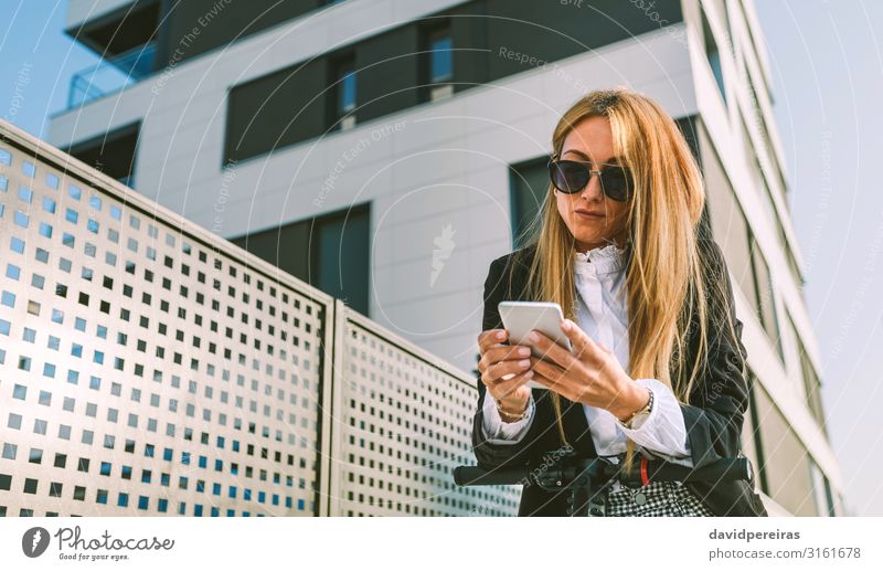 Geschäftsfrau lehnt auf ihrem Elektroroller und sieht auf der Straße mobil aus elegant PDA Mensch Frau Erwachsene Gebäude Mode Sonnenbrille blond modern