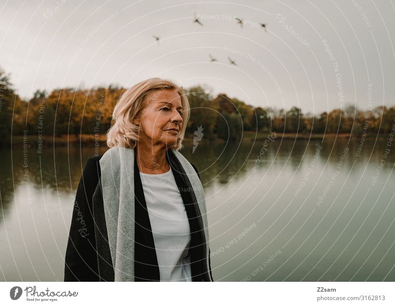 Traudl Lifestyle elegant Stil Weiblicher Senior Frau 60 und älter Natur Landschaft Herbst Schönes Wetter Baum Sträucher Seeufer T-Shirt Mantel Schal blond