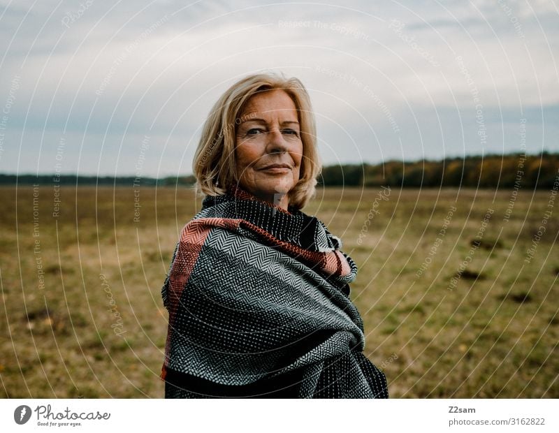60 jährige Dame mit Schal in Herbstlandschaft Stil Weiblicher Senior Frau 60 und älter Natur Landschaft Wolken Wiese Mantel Tuch blond Blick elegant Gesundheit