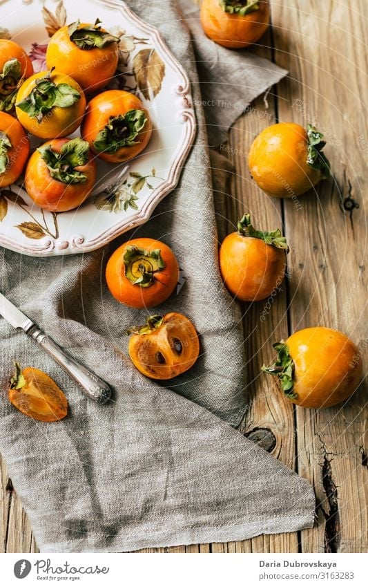 Schmackhafte, reife Kakipflaumen auf einem schönen Teller und Holztisch süß frisch geschmackvoll Persimone hölzern Gesundheit Dessert Ernährung orange