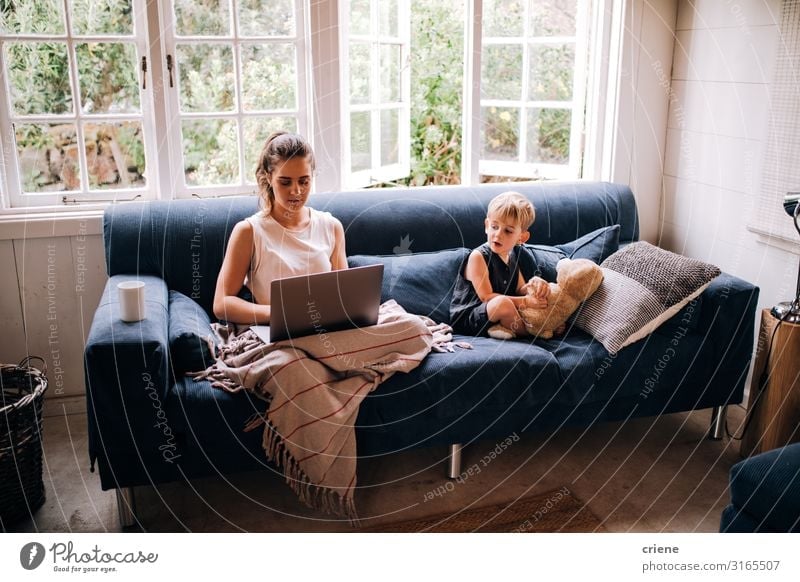 Mutter arbeitet am Laptop neben ihrem Sohn. Lifestyle Glück Erholung Freizeit & Hobby lesen Sofa Kind Arbeit & Erwerbstätigkeit Business Computer Notebook
