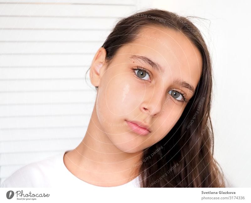 Porträt eines schönen, jungen, kaukasisch gebräunten Mädchens auf weißem Hintergrund in Nahaufnahme. Braunes langes gesundes Haar. Ruhiges Gesicht, Schönheitskonzept