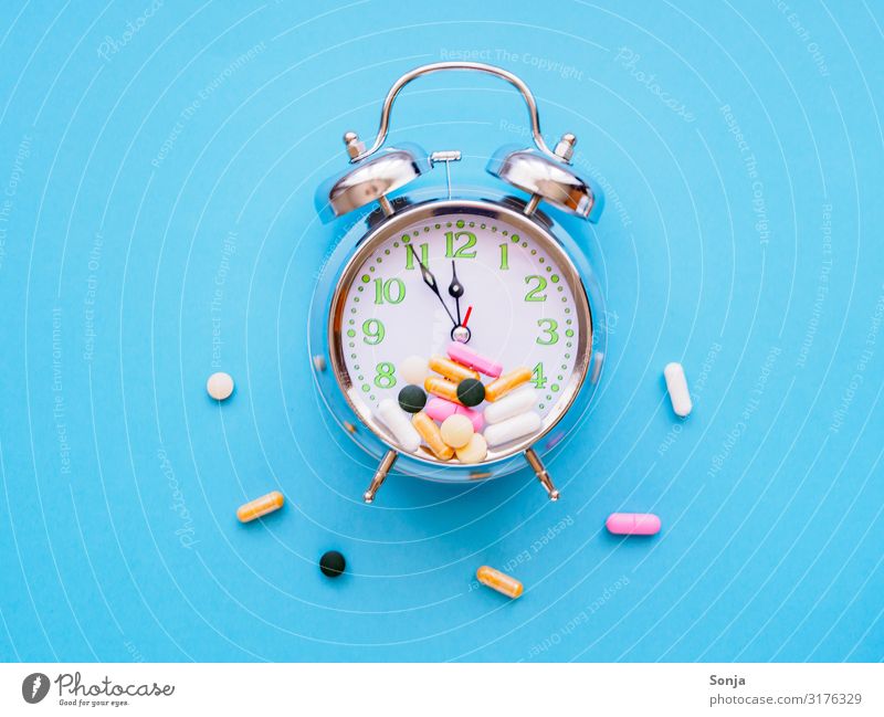 Wecker mit bunten Tabletten auf einem blauen Hintergrund Lifestyle Gesundheit Gesundheitswesen Seniorenpflege Uhrenzeiger Blauer Hintergrund Zeichen