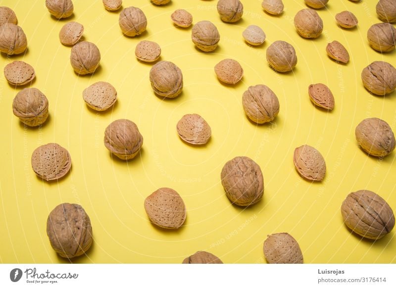 Nüsse und Mandeln auf gelbem Hintergrund Design Herbst Wärme braun Trockenfrüchte Lebensmittel Gesundheit Muttern Konsistenz Walnussholz Papier abstrakt Muster