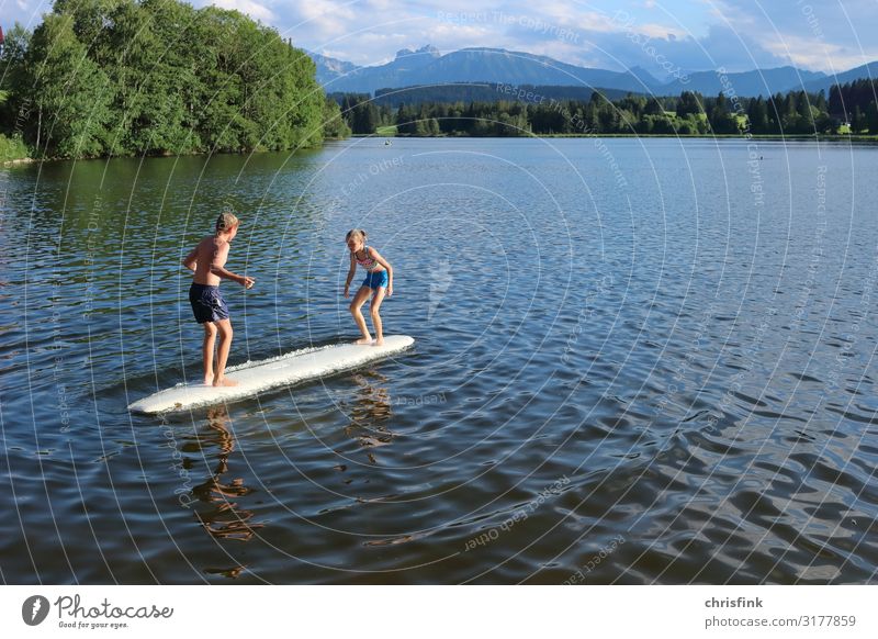 Kinder spielen auf Surfbrett in Bergsee Freizeit & Hobby Spielen Kinderspiel Ferien & Urlaub & Reisen Ausflug Wassersport Schwimmen & Baden Mensch