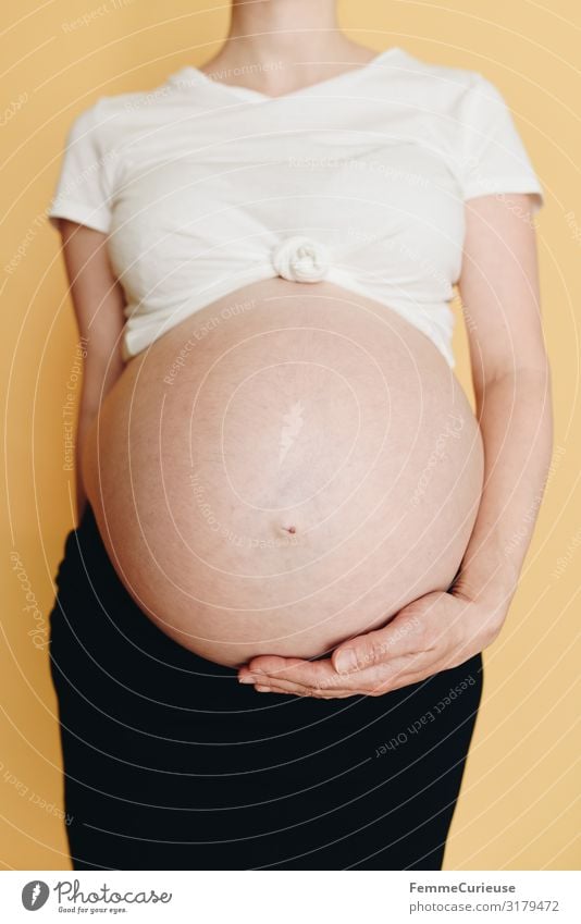 Schwangere Frau zeigt ihren Babybauch - neutraler Hintergrund feminin Erwachsene 1 Mensch 18-30 Jahre Jugendliche 30-45 Jahre Glück bauchfrei Magen Haut T-Shirt