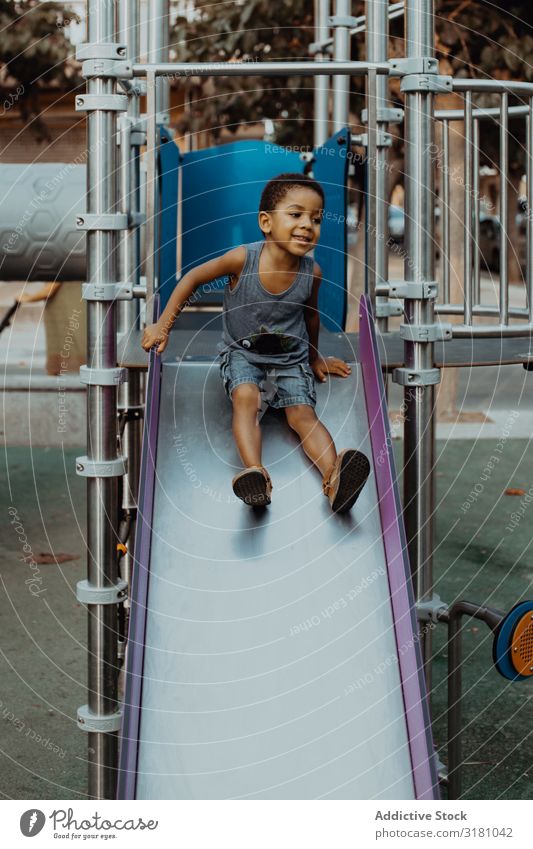 Lächelnder schwarzer Junge auf Rutsche Spielplatz Wegsehen Kind Freude Freizeit & Hobby Lifestyle ruhen Erholung Afroamerikaner urwüchsig Park Aktion unschuldig