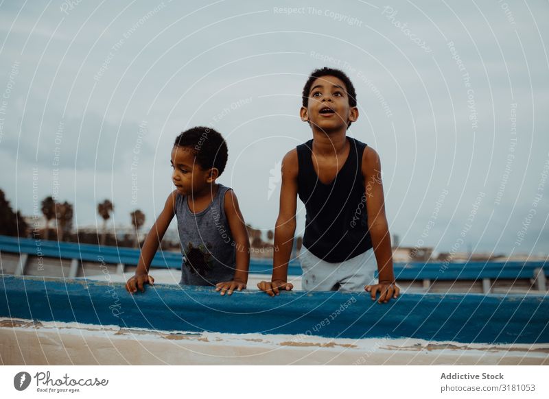 Erstaunte schwarze Jungs auf dem Boot Junge Wasserfahrzeug Strand erstaunt Wolken Himmel Zusammensein Freude anlehnen Gefäße Kind Geschwister Brüder