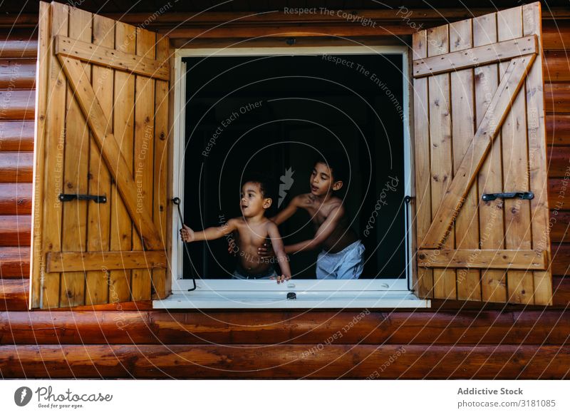 Schwarze Jungs schauen aus dem Fenster. Brüder Ausschau haltend Haus Holz offen Freude Zusammensein Afroamerikaner Kind Junge Geschwister ohne Hemd Fensterladen