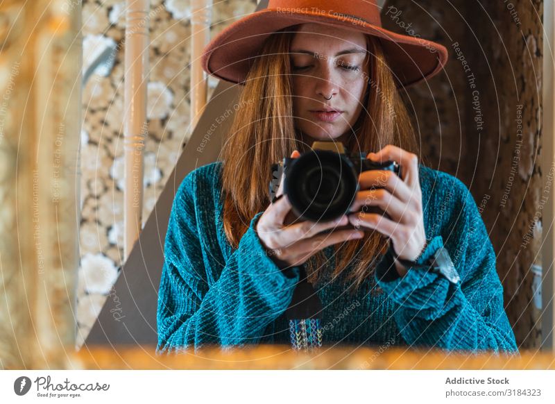 Junge Frau beim Fotografieren zu Hause heimwärts professionell Fotokamera Spiegel expressiv Jugendliche rothaarig schön modern Pullover Hut attraktiv charmant