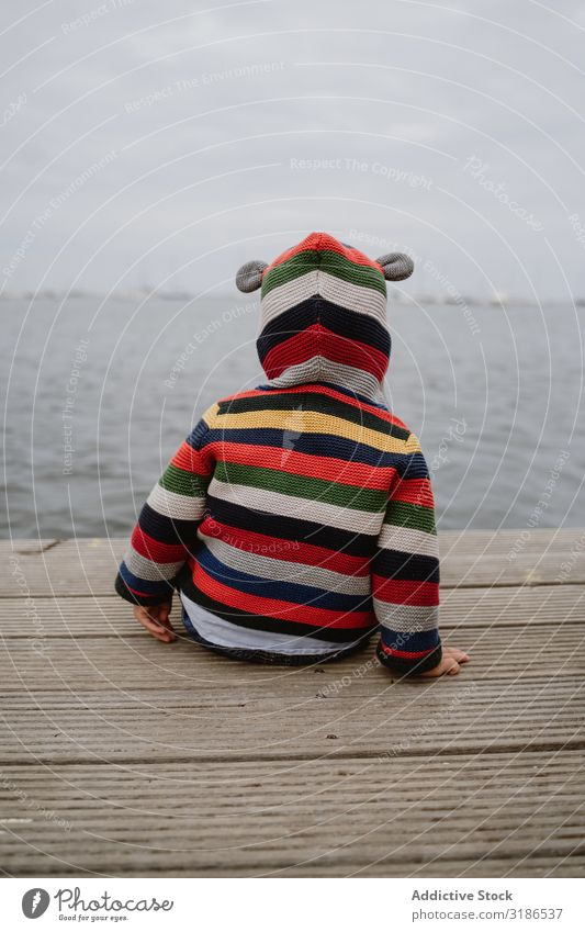 Anonymes Kind auf dem Pier sitzend Anlegestelle Meer Baby lässig Lifestyle Freizeit & Hobby ruhen Erholung gestreift Jacke Motorhaube marin Wasser Küste klein