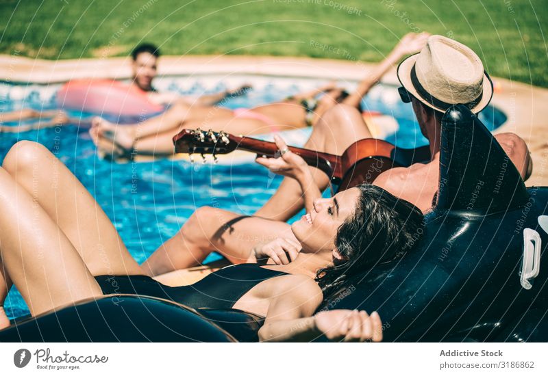 Männer und Frauen entspannen sich am Pool. Schwimmbad Schwimmsport Freundschaft Gitarre Spielen Instrument Mann Luftmatratze gutaussehend Glück heiter